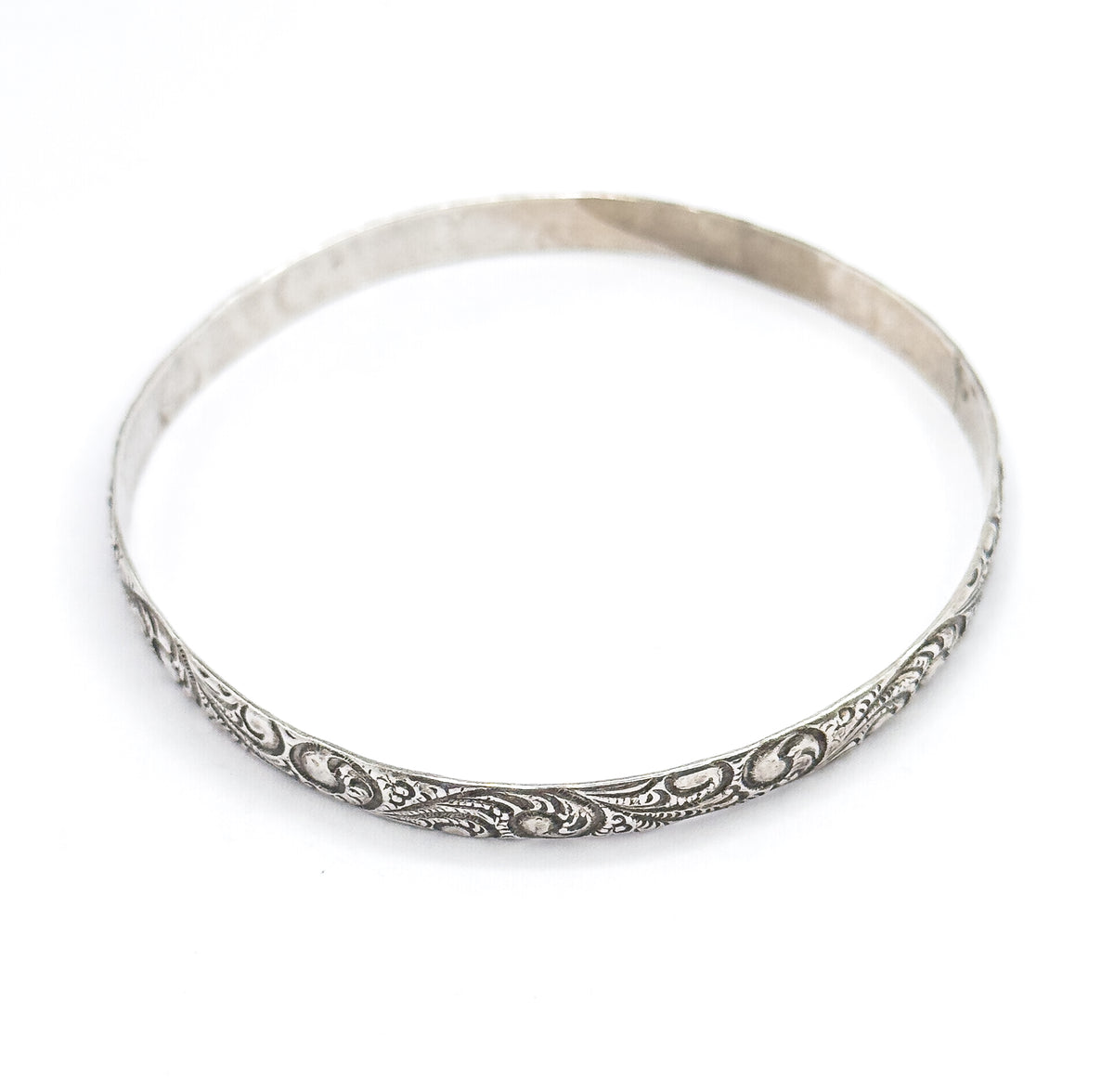 Angled view of the bangle standing on a plain background, so the full depth of the band is visible with the scrollwork curving along the near side and the smooth edge rising behind.