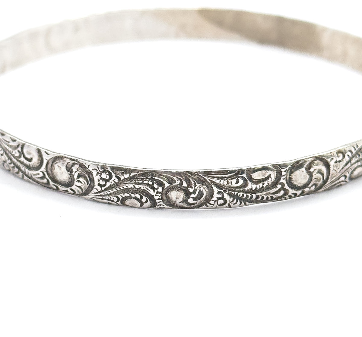 Tight macro crop of the lower front of the band, filling the frame so individual raised scrolls and the darkened patina settled in their recesses can be read in detail.