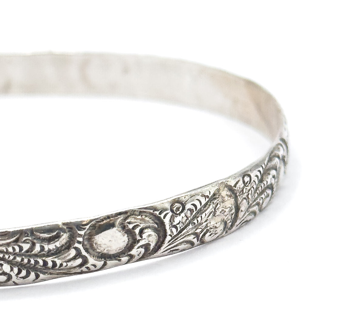 Close view of one curving section of the band where the raised scrollwork tapers away into the plain polished surface, with the smooth inner wall of the bangle visible behind.