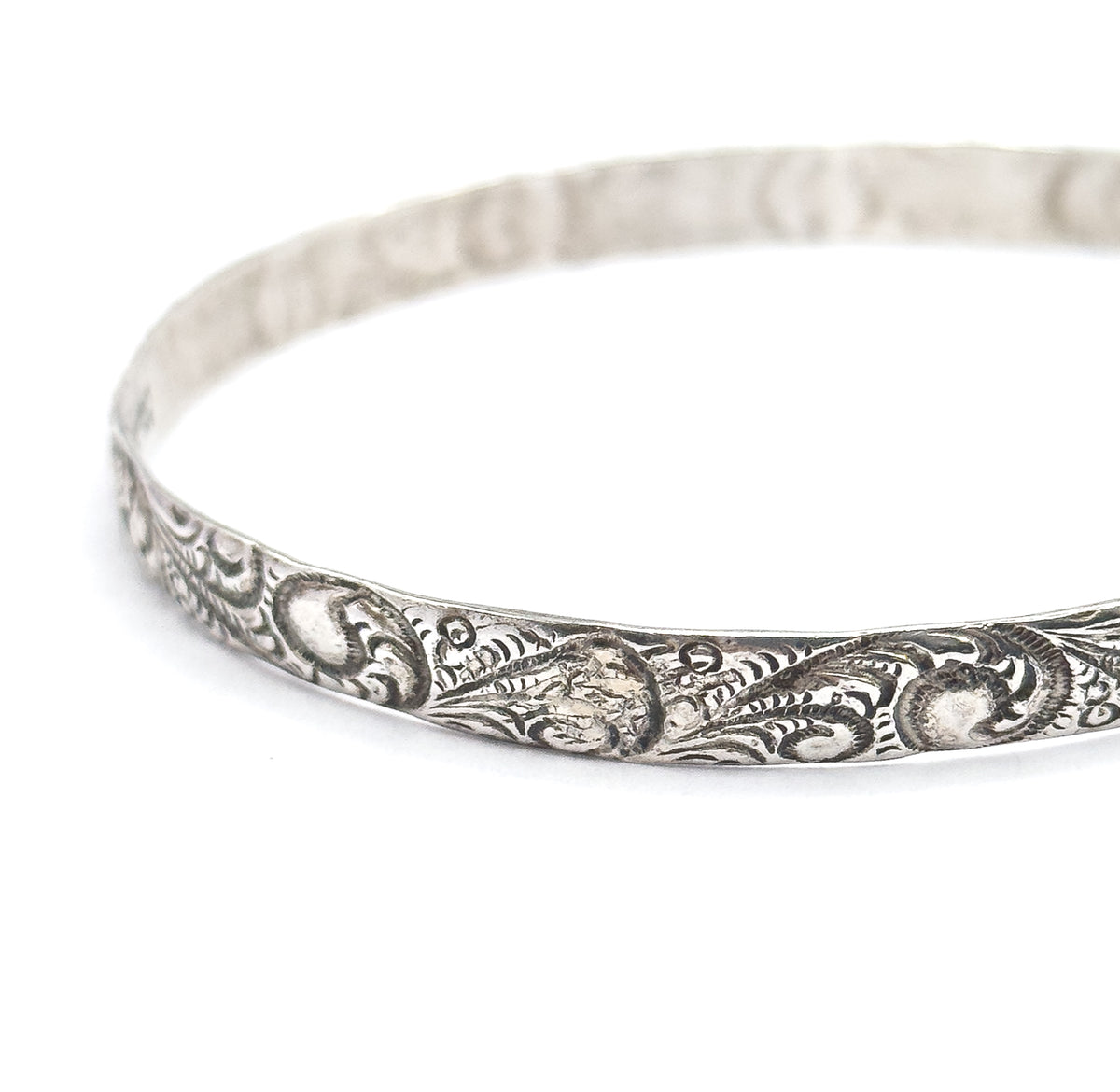 Steeply tilted view with the bangle cropped at the right edge, the open oval reading clearly as a ring and the scroll pattern carrying unbroken along the near rim into soft focus at the back.
