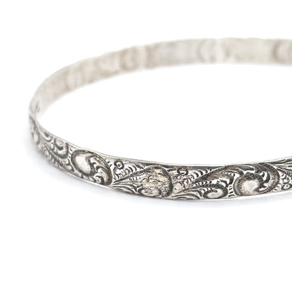 Steeply tilted view with the bangle cropped at the right edge, the open oval reading clearly as a ring and the scroll pattern carrying unbroken along the near rim into soft focus at the back.
