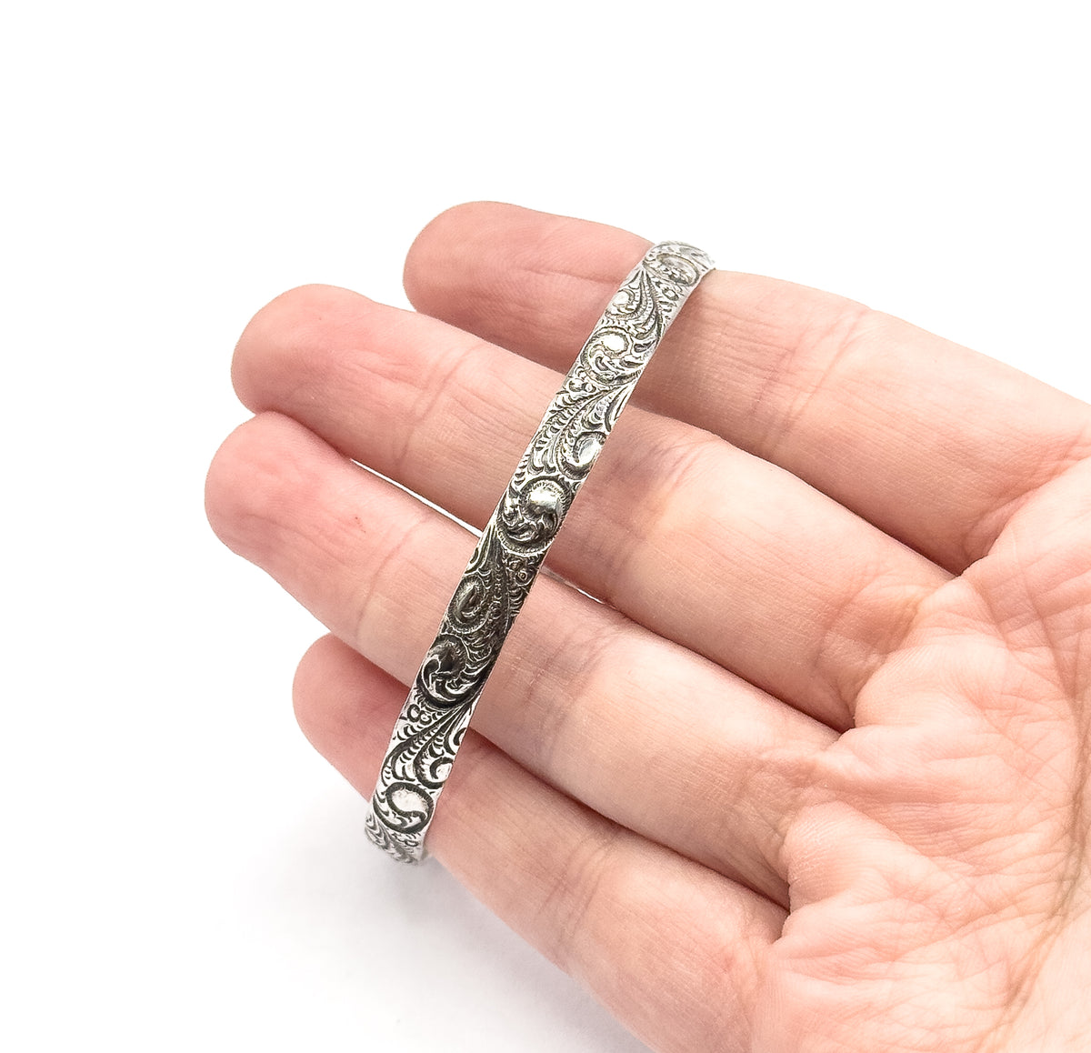 Sterling silver scroll pattern bangle resting diagonally across the fingers of an open hand, its raised scrollwork and dark patina in the recesses giving a sense of the band's width.