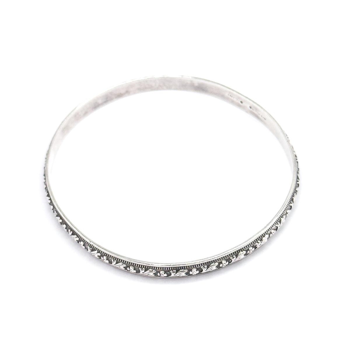 The full circle of the bangle seen from above against a white background, with the carved flower-and-leaf band and beaded borders running along the lower rim and a stamp visible inside the upper curve.