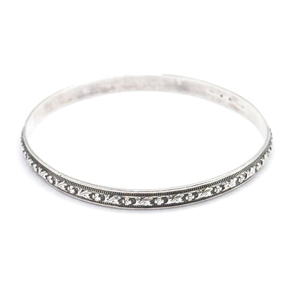 The bangle tilted lower so the carved flower-and-leaf station and its beaded borders run across the front rim, with the smooth inner wall and faint stamp visible at the back.