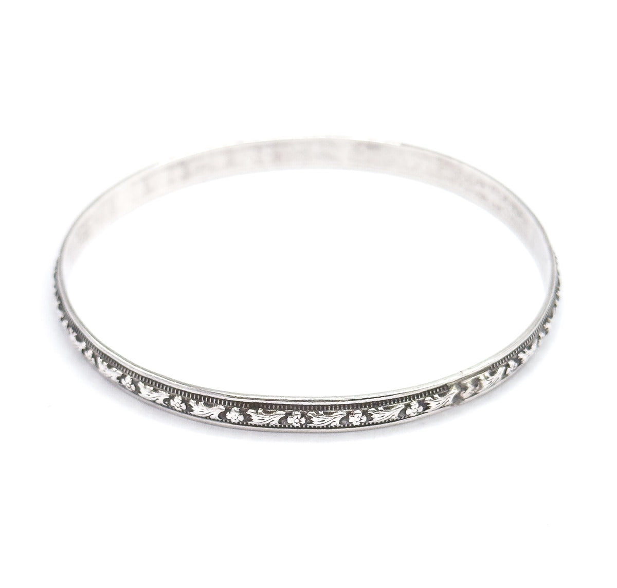 The complete oval of the bangle seen from slightly above, the carved floral station and beaded borders running the full length of the near rim while the plain polished band sweeps round behind.