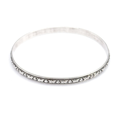 The complete oval of the bangle seen from slightly above, the carved floral station and beaded borders running the full length of the near rim while the plain polished band sweeps round behind.