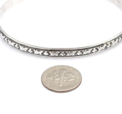 A ten-cent coin placed below the bangle gives the scale, showing the carved flower-and-leaf band and its beaded borders as only a little wider than the coin's rim.