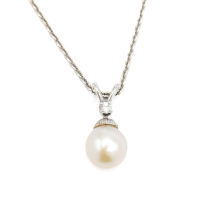 Straight-on front view against white with the chain sweeping up in a wide V from the looped bail, the diamond centred above the fluted cap and the round creamy pearl hanging below.