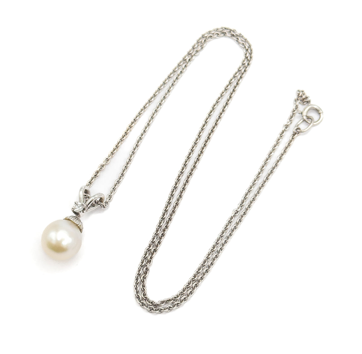 The whole necklace laid out flat, the doubled chain looping down the frame to the spring-ring clasp at upper right, with the pearl pendant and its diamond-set bail at lower left.