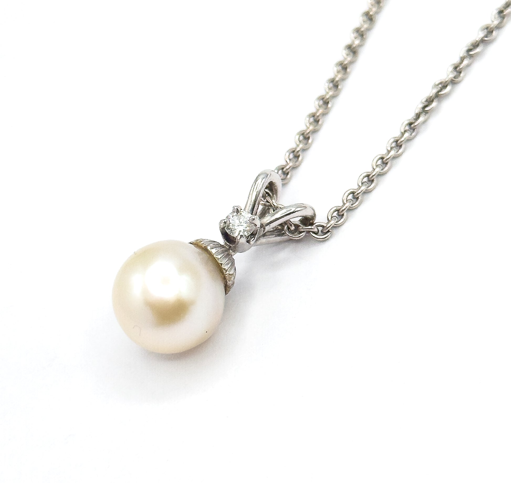 Side view against white showing the ridged cap where the pearl meets its white gold mount, the diamond above it in profile and the chain running off to the upper right.