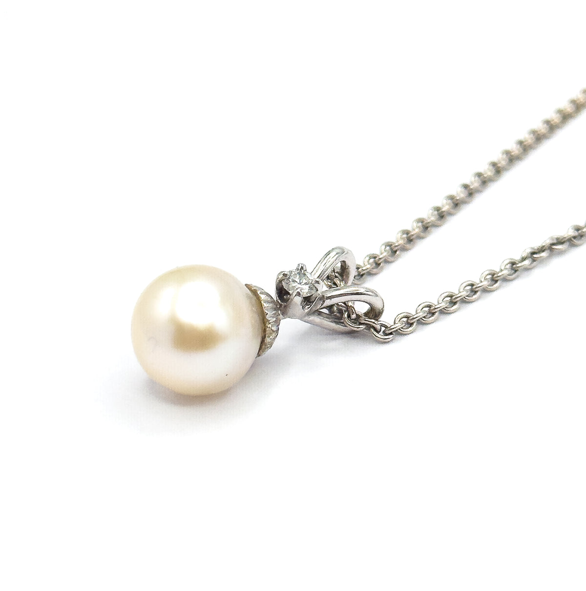 Three-quarter view from below, the fluted cap and looped bail seen from underneath with the diamond glinting through the ribbon opening and the chain rising to the right.