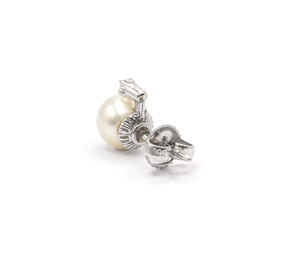 A single earring tilted upward so the rounded pearl profile, the fluted buttercup gallery and the diamond prongs read at once, with its post back pushed onto the end of the post.