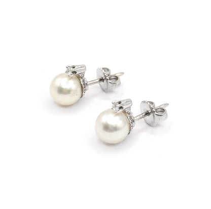 Seen from behind and above, both earrings lie diagonally with pearls at the left and the fluted buttercup caps turned away, each post running back through its butterfly back.