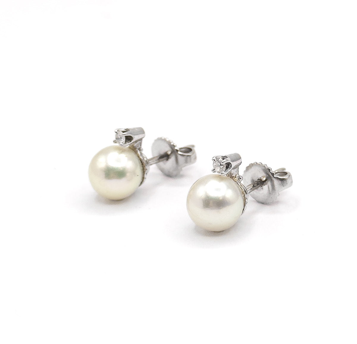 Both earrings in low side profile, one behind the other, so the pearls and diamond-topped buttercup caps sit at the left and each post stretches right into its butterfly back at eye level.