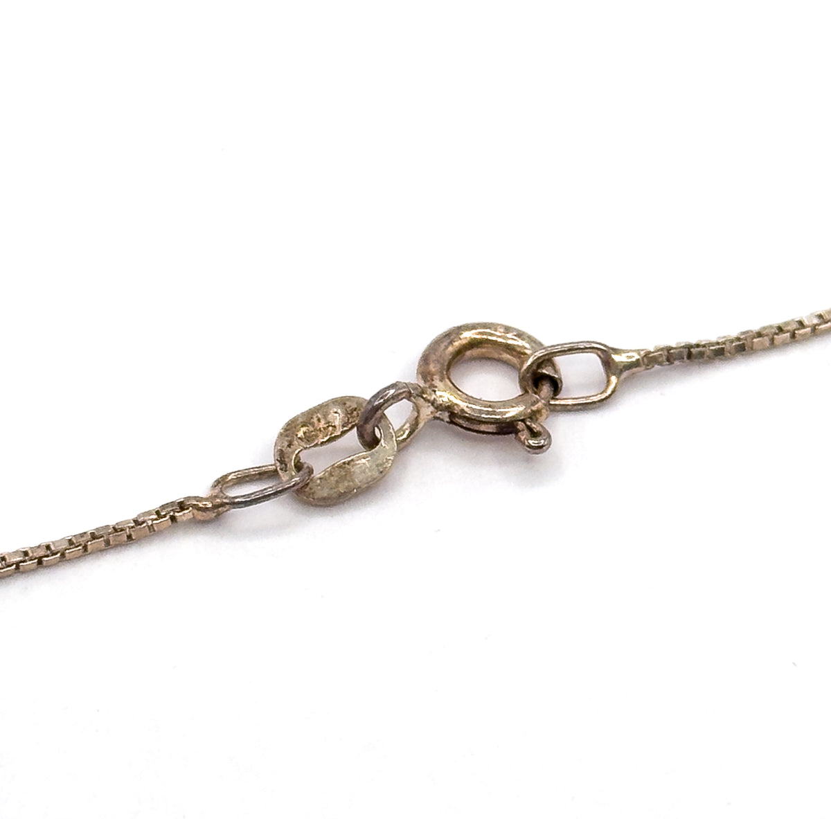 Close view of the spring ring clasp and its oval jump rings at the end of the silver box chain, laid against a white background.
