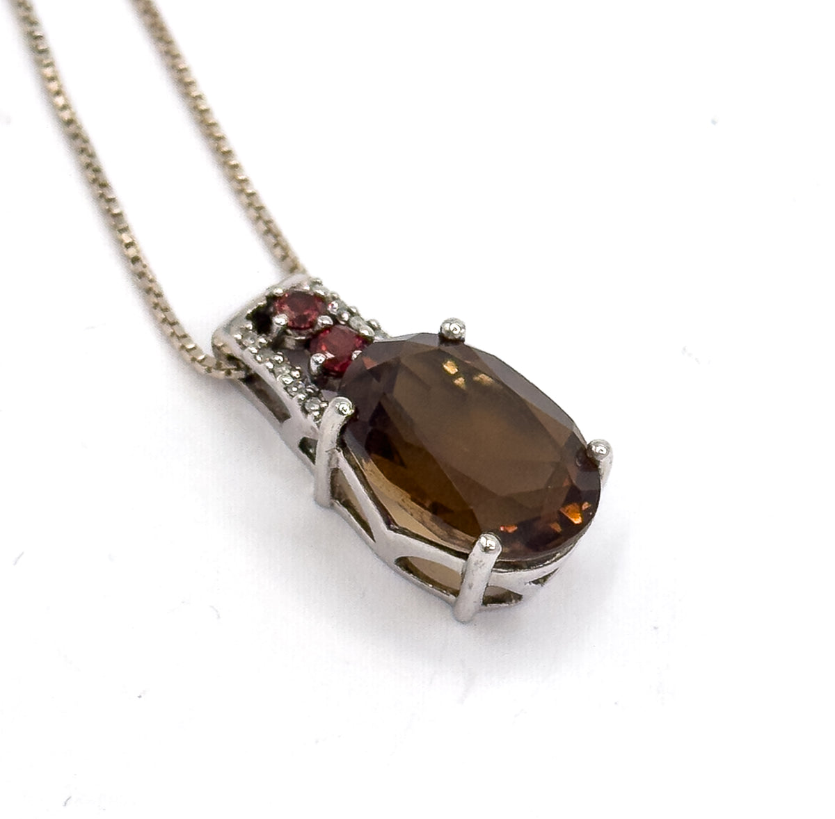 Tight close-up of the pendant head from above, showing the open basket gallery under the oval quartz and the bar of two garnets beside tiny clear stones.