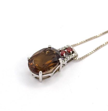 Diagonal view from above with the pendant at lower left and the box chain running off to the upper right, the quartz tilted so light pools in its table and the two garnets face the viewer.