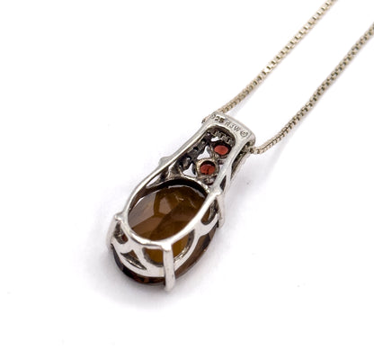 Silver pendant necklace shown from the back at an angle, the open basket setting cradling the oval quartz with two round garnets above, the box chain trailing off to the upper right.
