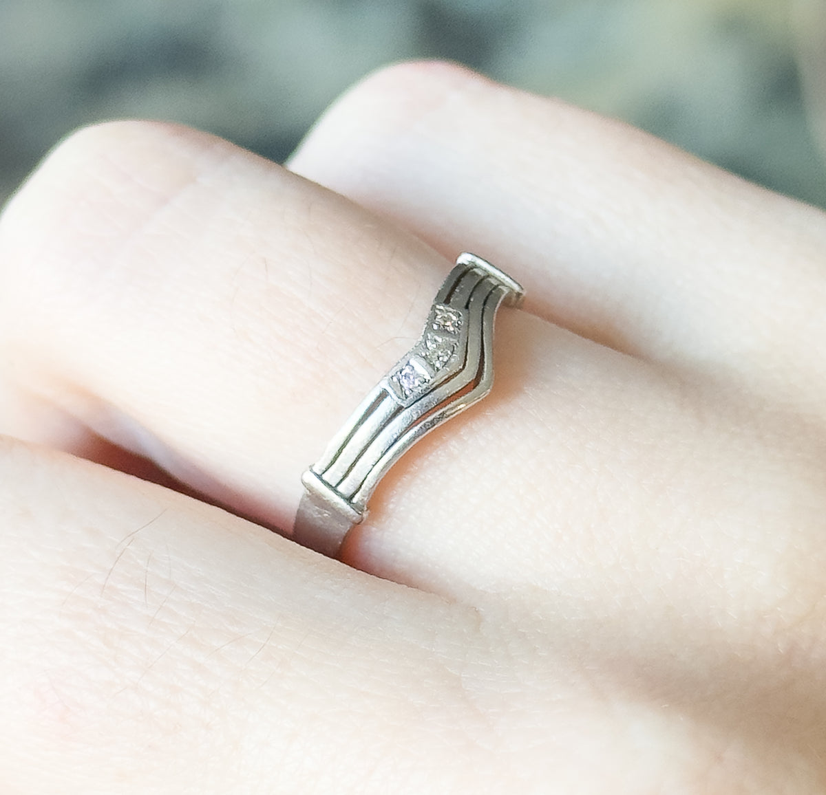 Close side view of the chevron band shown on a finger, its ribbed shank curving up to the V where the three small diamonds catch the light.