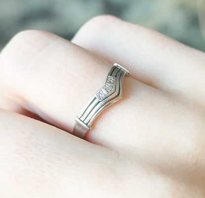 Close side view of the chevron band shown on a finger, its ribbed shank curving up to the V where the three small diamonds catch the light.
