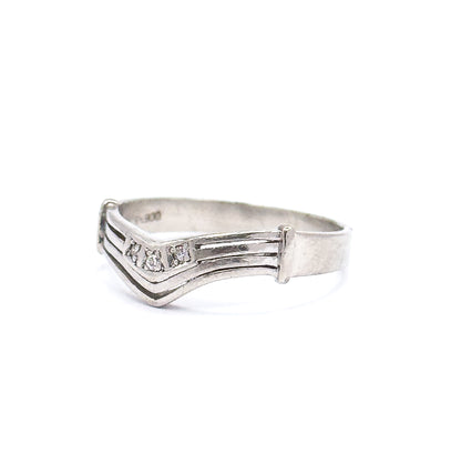Low three-quarter view from the front, the chevron point tilted toward the viewer so the three small diamonds catch light between the parallel grooves and the flat end caps.