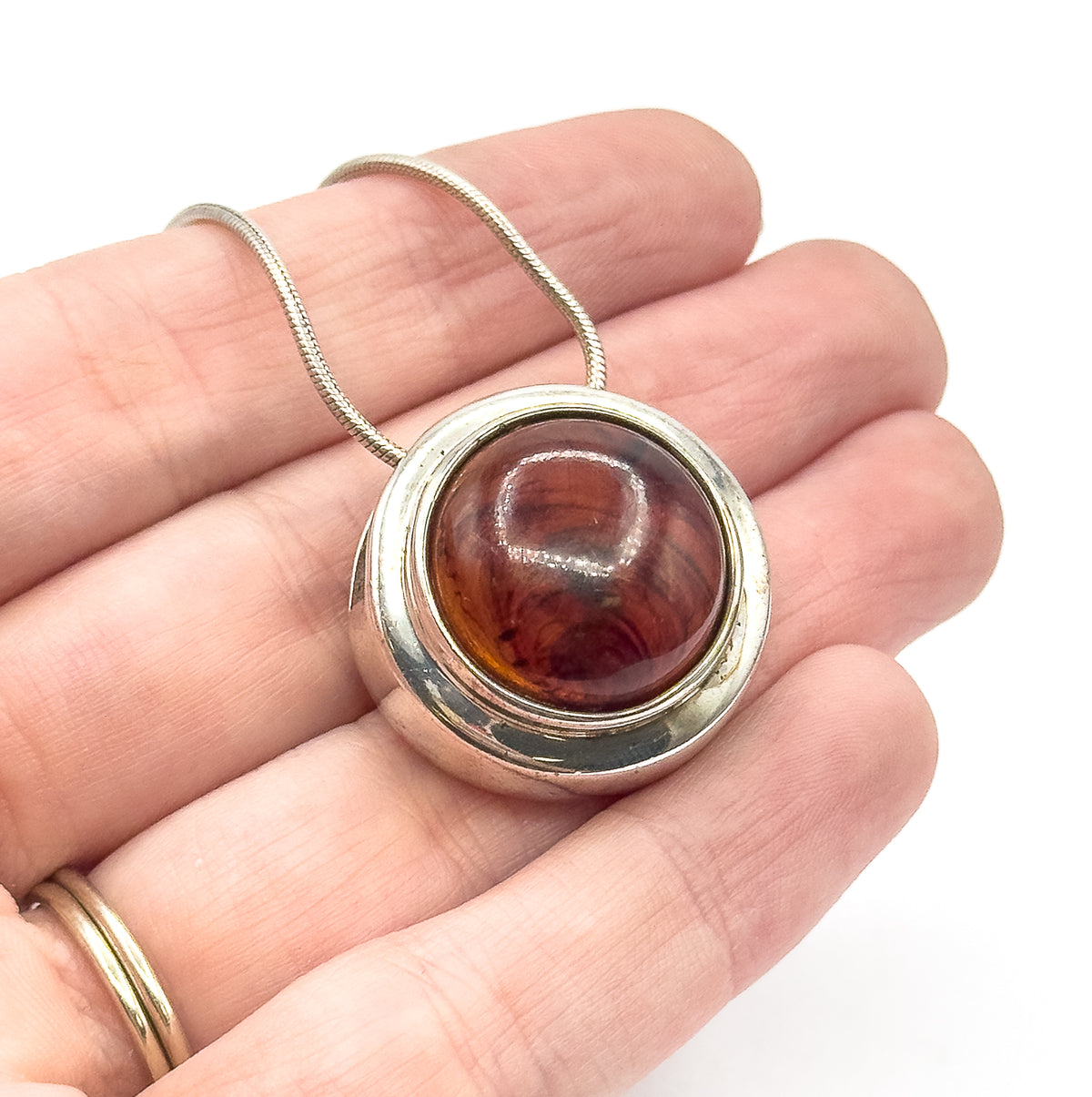 The pendant shown resting on open fingers, giving a sense of its size, with the snake chain draped across the hand behind it.