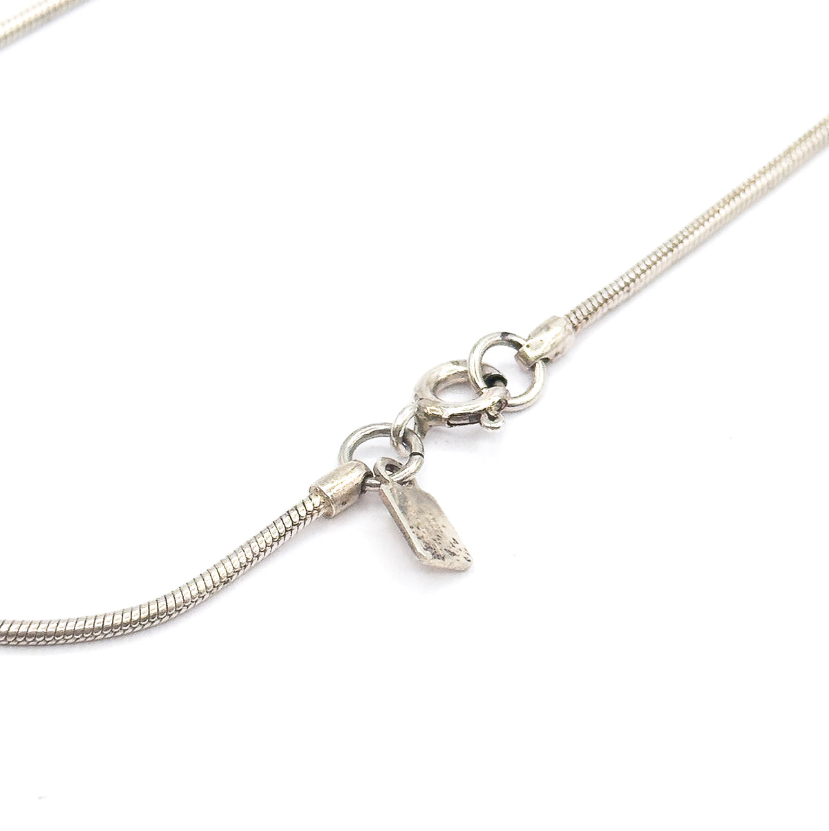 Close view of the sterling silver snake chain's spring ring clasp, with the small stamped tag hanging beside it on white.