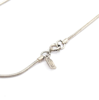 Close view of the sterling silver snake chain's spring ring clasp, with the small stamped tag hanging beside it on white.