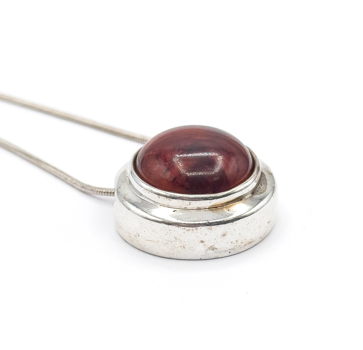 Angled three-quarter view showing the pendant's deep cylindrical side wall and stepped bezel rim, with the domed resin cabochon and its dark swirls catching the light.