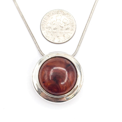 The pendant photographed beside a dime for scale, the coin roughly half the width of the round bezel, with the snake chain running behind both.