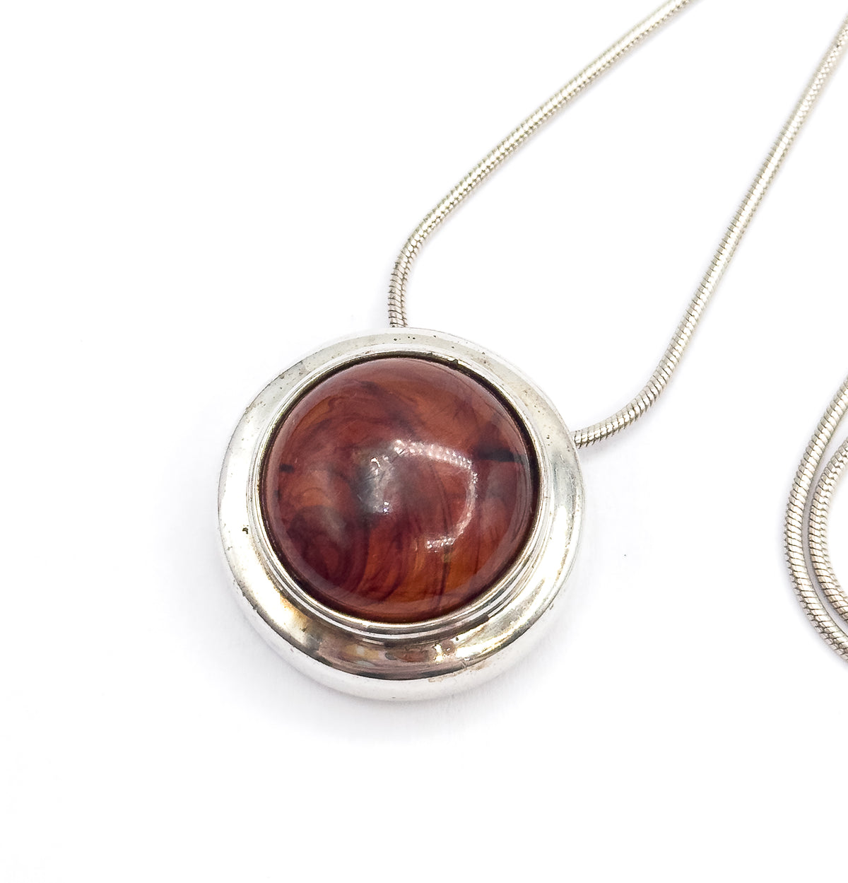 Tilted front view with the snake chain sweeping off to one side and curling into a loop, the domed resin cabochon set deep in its polished sterling silver bezel.