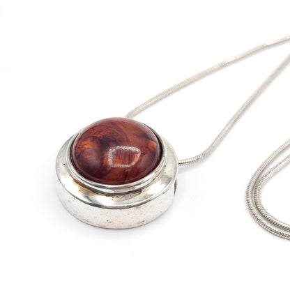 Low angled view from above the pendant's rim, showing the slide channel opening at the side of the deep sterling silver wall, with the snake chain looping in a long double curve to the right.