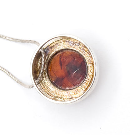 Sterling silver slide pendant set with a round amber-coloured resin cabochon in a raised bezel, shown flat from above on white with its snake chain curving away to the left.
