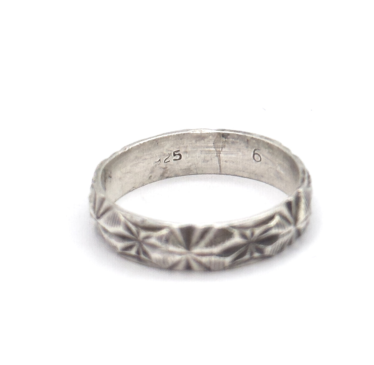 Standing upright on a plain white background, the band shows its starburst facet pattern across the front and the small stamped marks inside the shank.