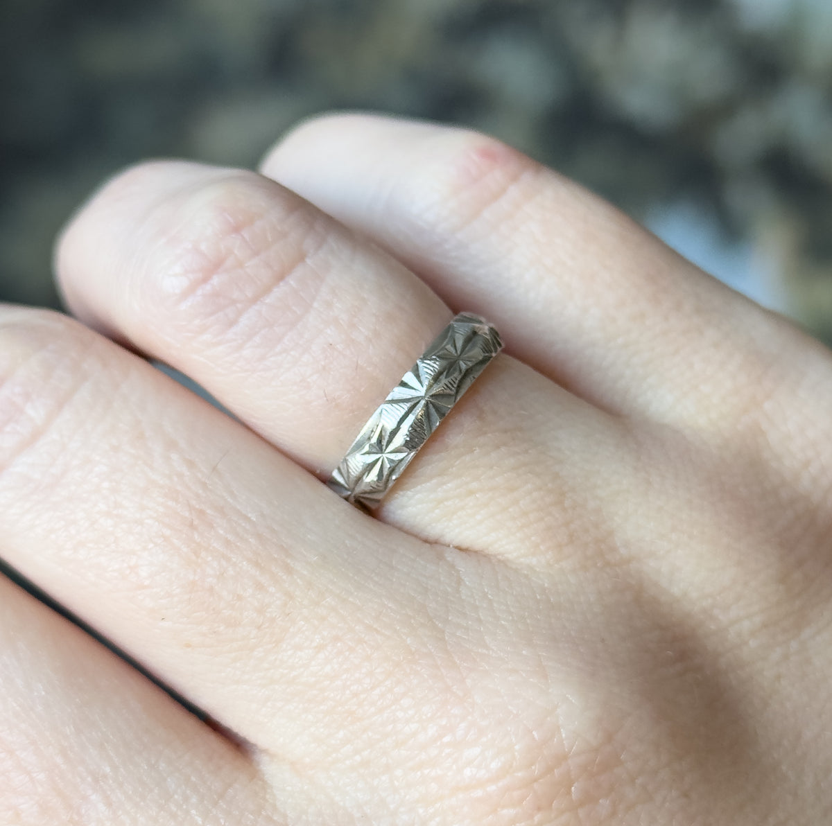Sterling silver textured band ring, shown on a finger, its diamond-cut faceted surface and coin-edge borders catching the light against the skin.