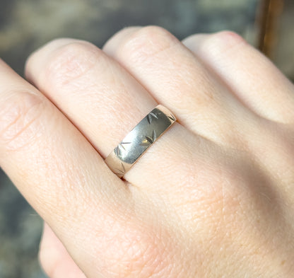 Shown on a finger from above, the band's star-like diamond cut facets catching light across the smooth sterling silver surface, with the hand filling the frame for scale.