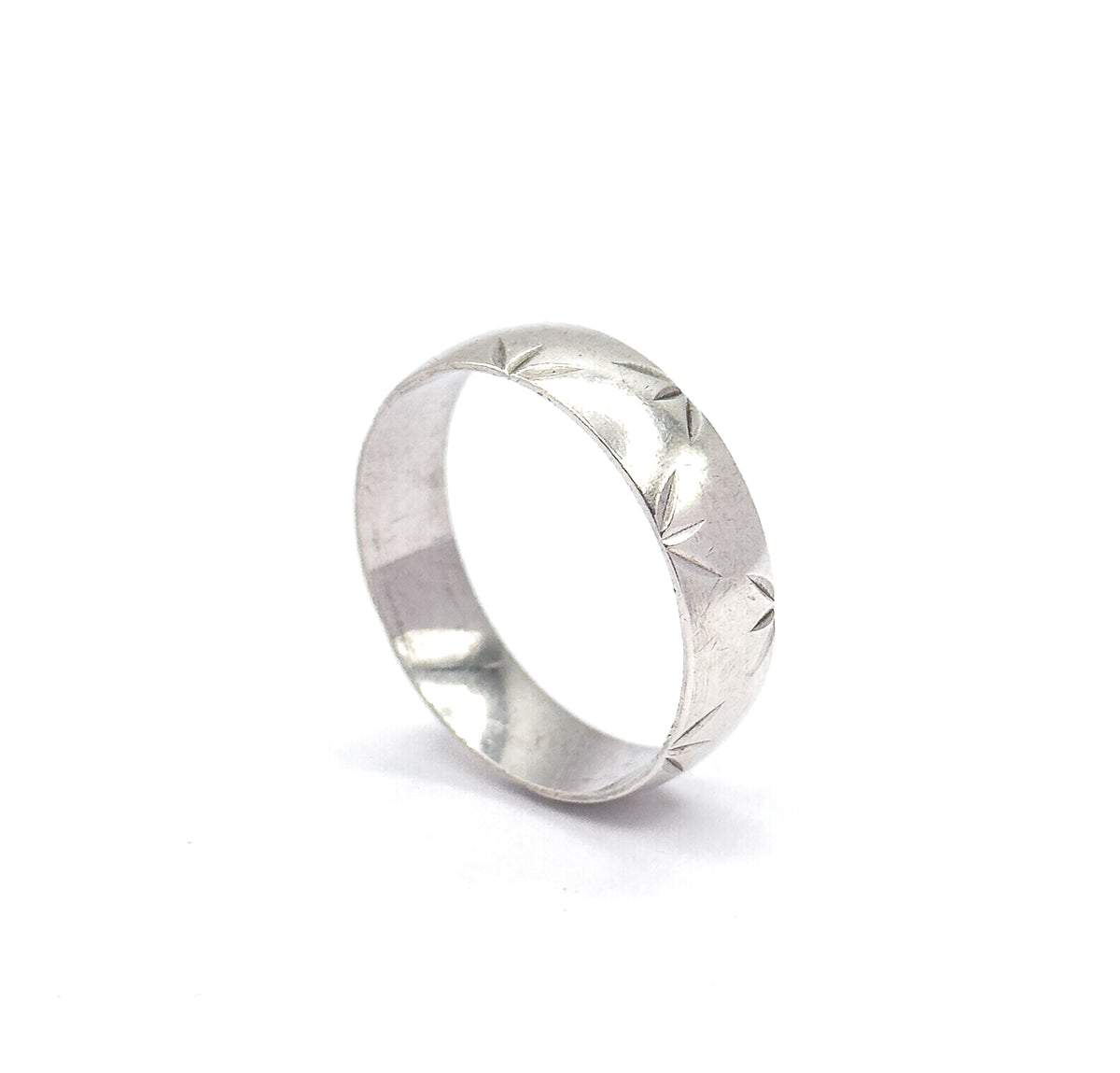 The band off the hand and standing upright on a white background, tilted so the star-cut facets along the outer face and the smooth inner shank are both visible.