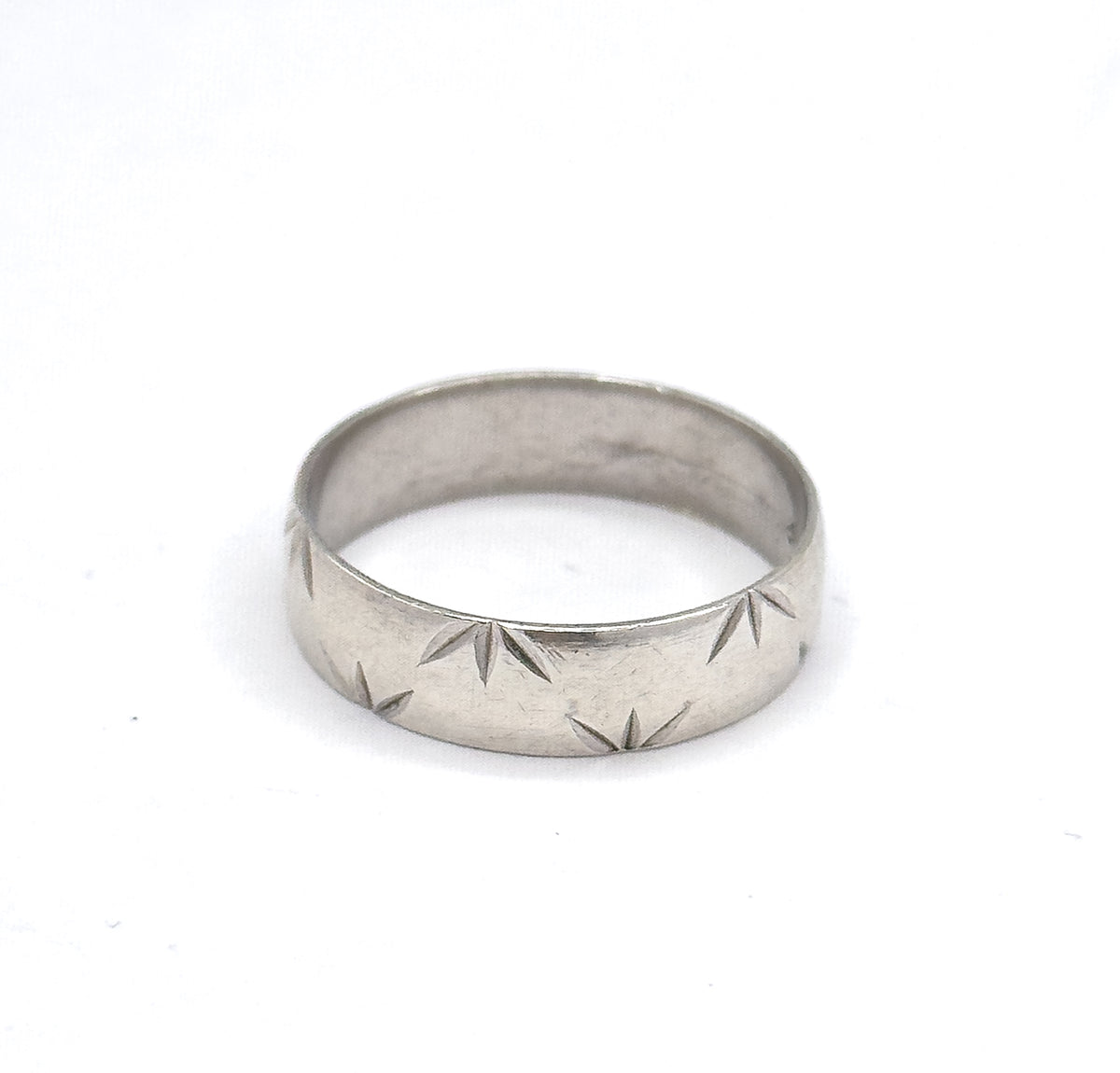 Seen low and nearly straight on against white, the band leans slightly away so the row of star-cut facets spreads across the front of the shank with the smooth inner wall in shadow behind.