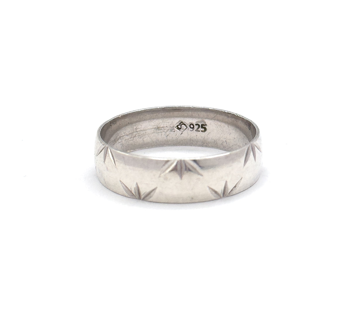 Set small in a wide white field, the band tilts just enough to show the stamped marks inside the shank while the star cuts step along the lower edge of the outer wall.