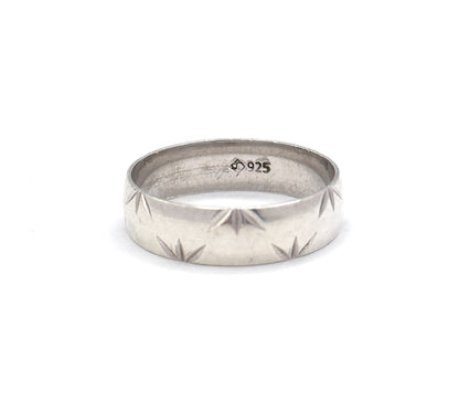 Set small in a wide white field, the band tilts just enough to show the stamped marks inside the shank while the star cuts step along the lower edge of the outer wall.