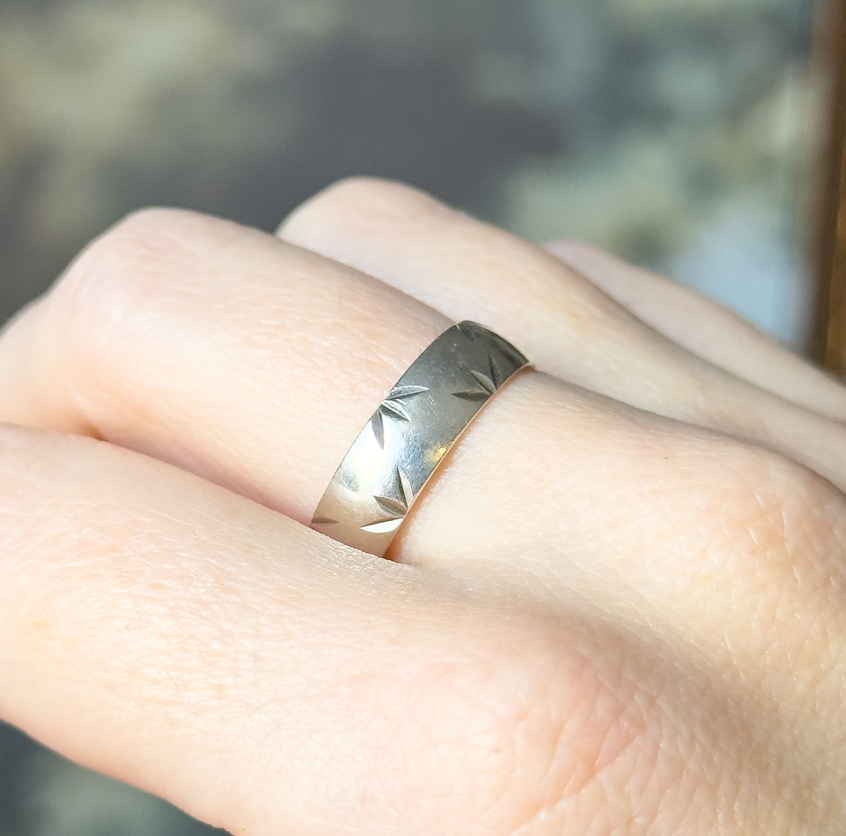 A Mid-Century sterling silver band with a diamond cut pattern along its width, shown on a finger so its broad, smooth shank can be judged against the hand.