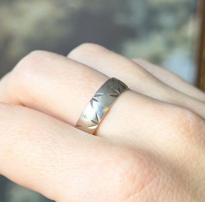 A Mid-Century sterling silver band with a diamond cut pattern along its width, shown on a finger so its broad, smooth shank can be judged against the hand.