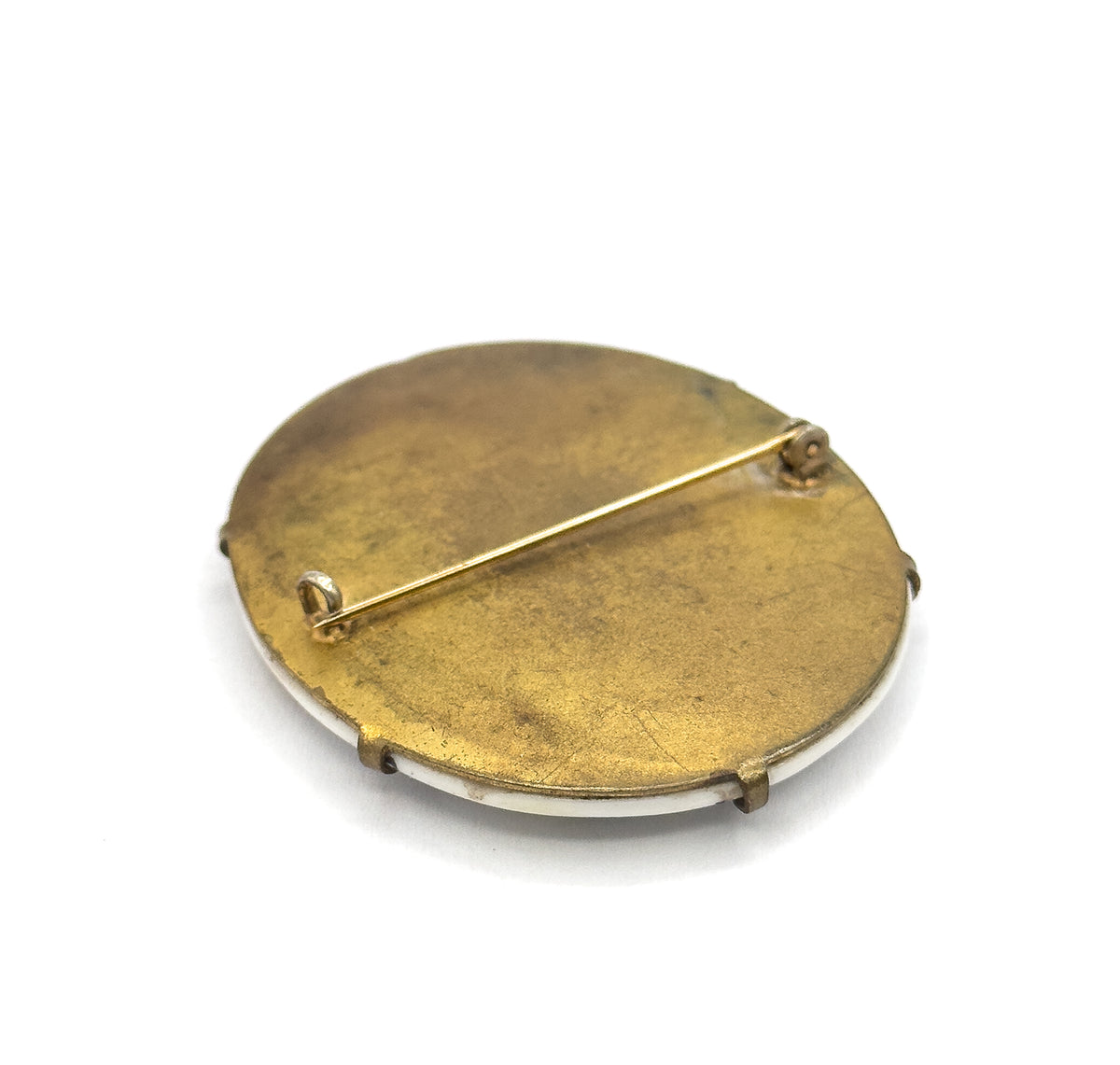 The reverse, angled on a white background, showing the plain base metal back with a long pin stem running between its hinge and catch, and the prongs folding over the pale plaque edge.