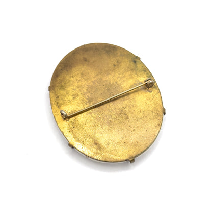 A flatter overhead view of the same back, the pin stem lying closed across the oval from its hinge to the small catch, with prong tips showing at the rim.