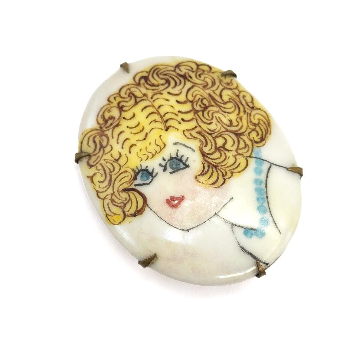 Viewed almost square-on from the front, the full oval fills the frame so the painted curls, blue eyes, red lips and bead strand are all legible at once, with six prong tips spaced round the rim.