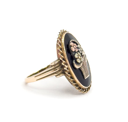 Angled three-quarter view from the side and slightly above, showing the flowers standing proud of the black stone above the ribbed basket, with the rope border curving away toward the shank.