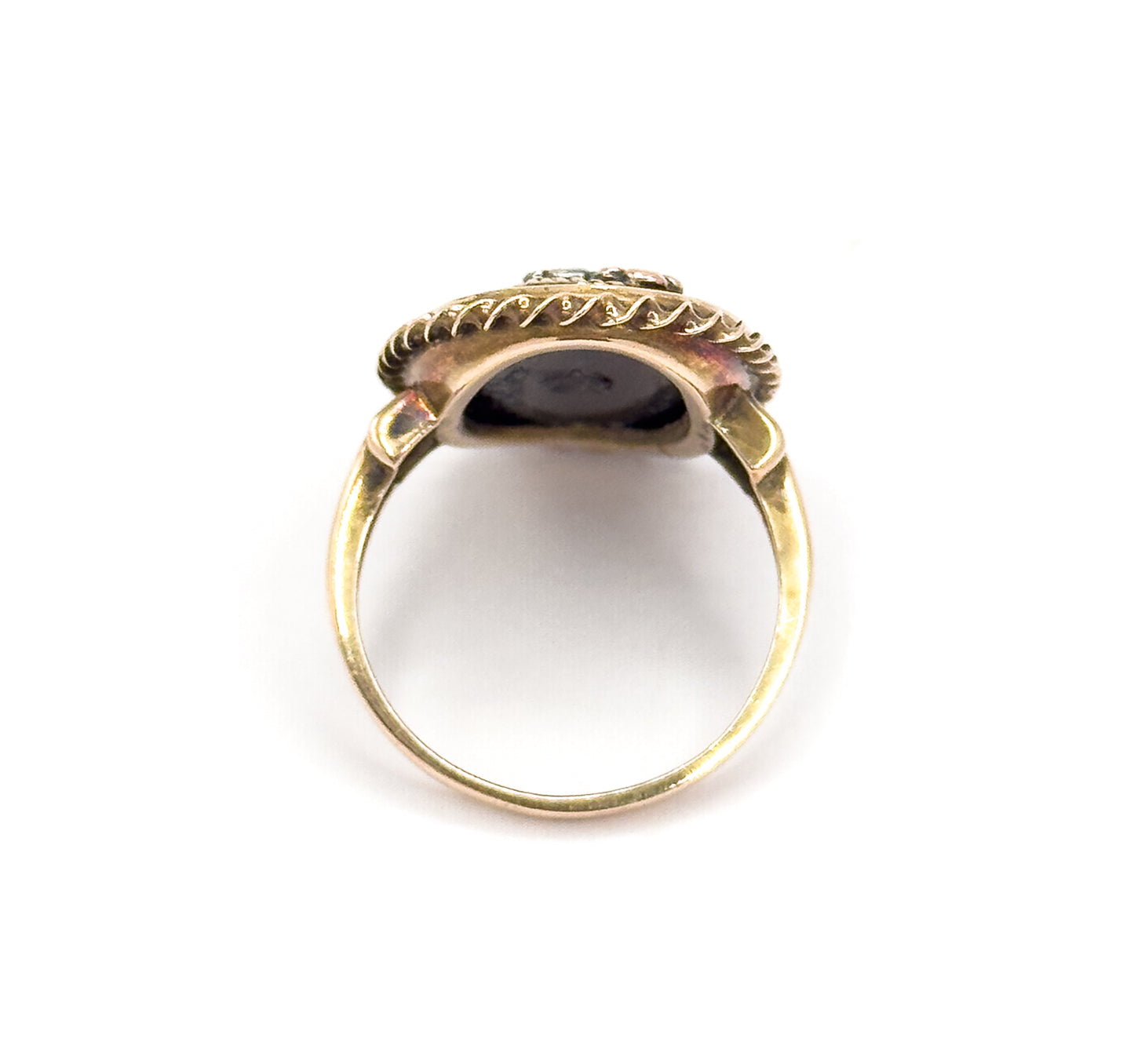 Viewed from behind the head against white, looking through the open circle of the plain shank up to the underside of the bezel, with the rope border and flower tips cresting the top.