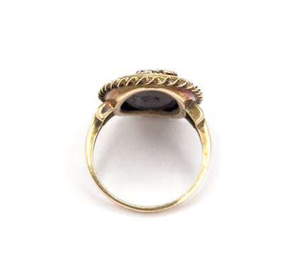 Viewed from behind the head against white, looking through the open circle of the plain shank up to the underside of the bezel, with the rope border and flower tips cresting the top.