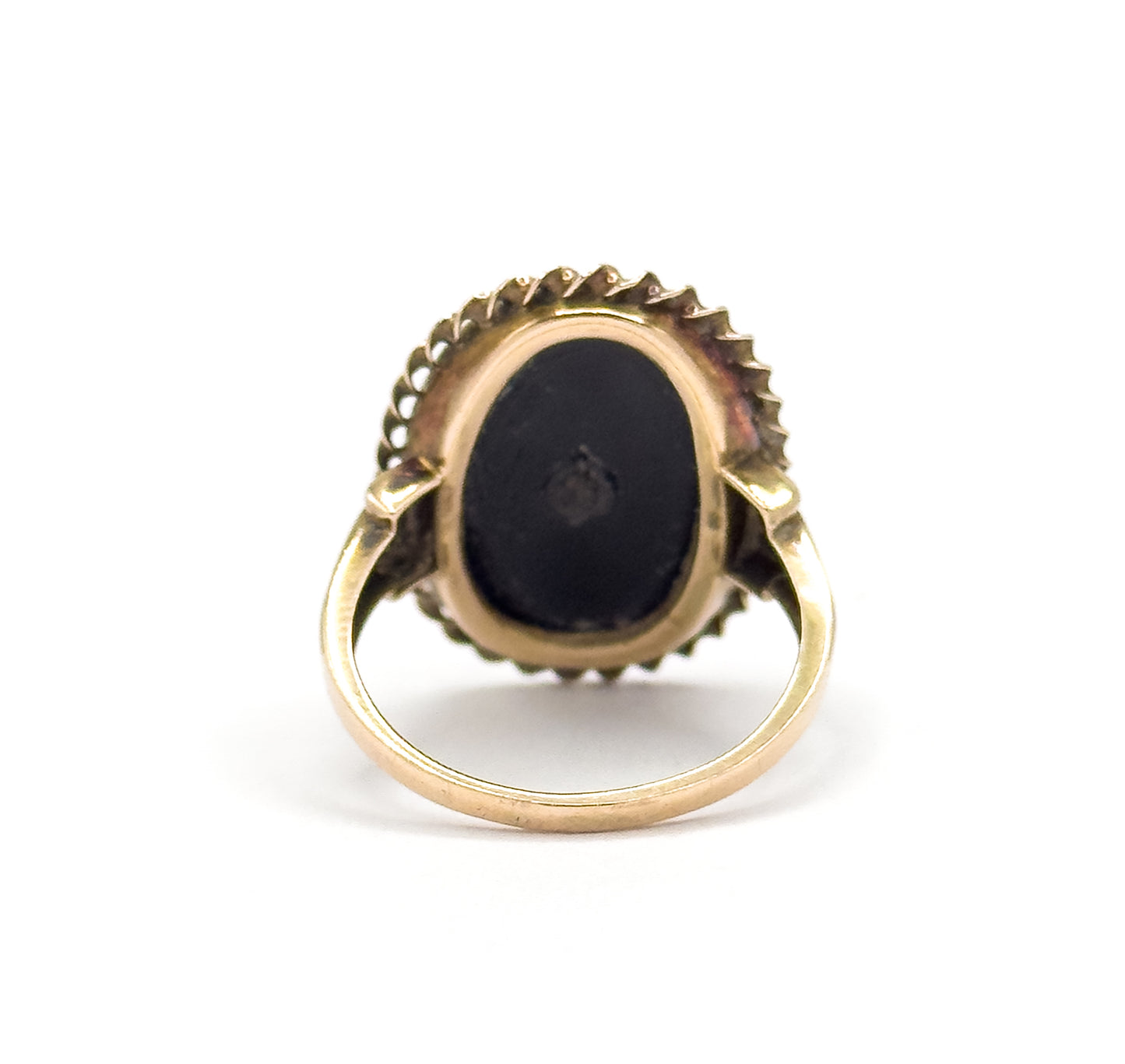 Reverse of the head against white, the flat dark back of the stone filling its open bezel with the rope border and flower tips ringing the edge, and the plain shank rising into split shoulders.