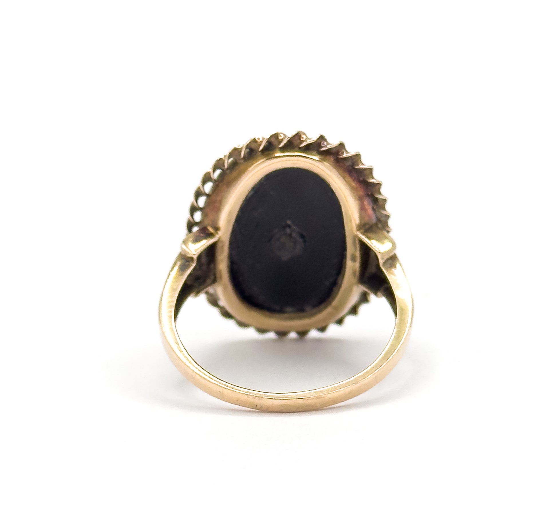 Reverse of the head against white, the flat dark back of the stone filling its open bezel with the rope border and flower tips ringing the edge, and the plain shank rising into split shoulders.